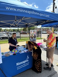 One CPED staff member talking to people about Minneapolis 2050, under a blue tent at an outdoor community event